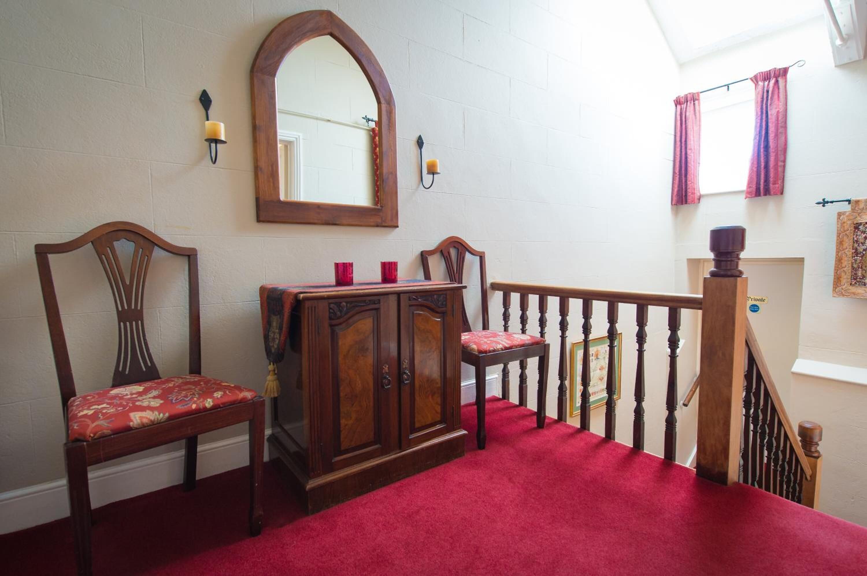 Una escalera con alfombra roja, sillas de madera, un armario de madera y un espejo en la pared.