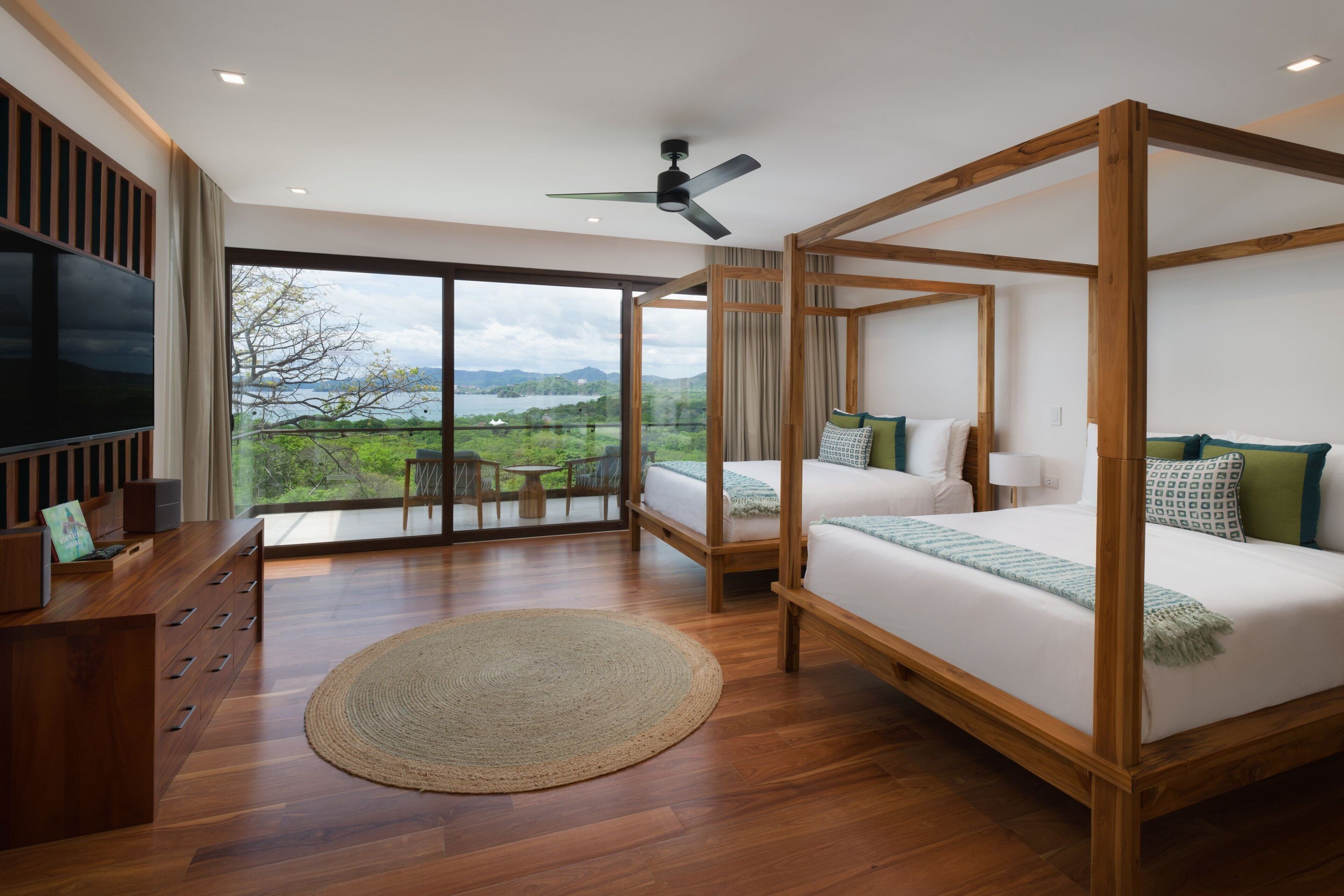A spacious bedroom with a large bed, a TV, and a balcony with a view of the outdoors.