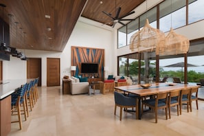 A modern kitchen with a wooden ceiling, a large dining table, and a TV mounted on the wall.