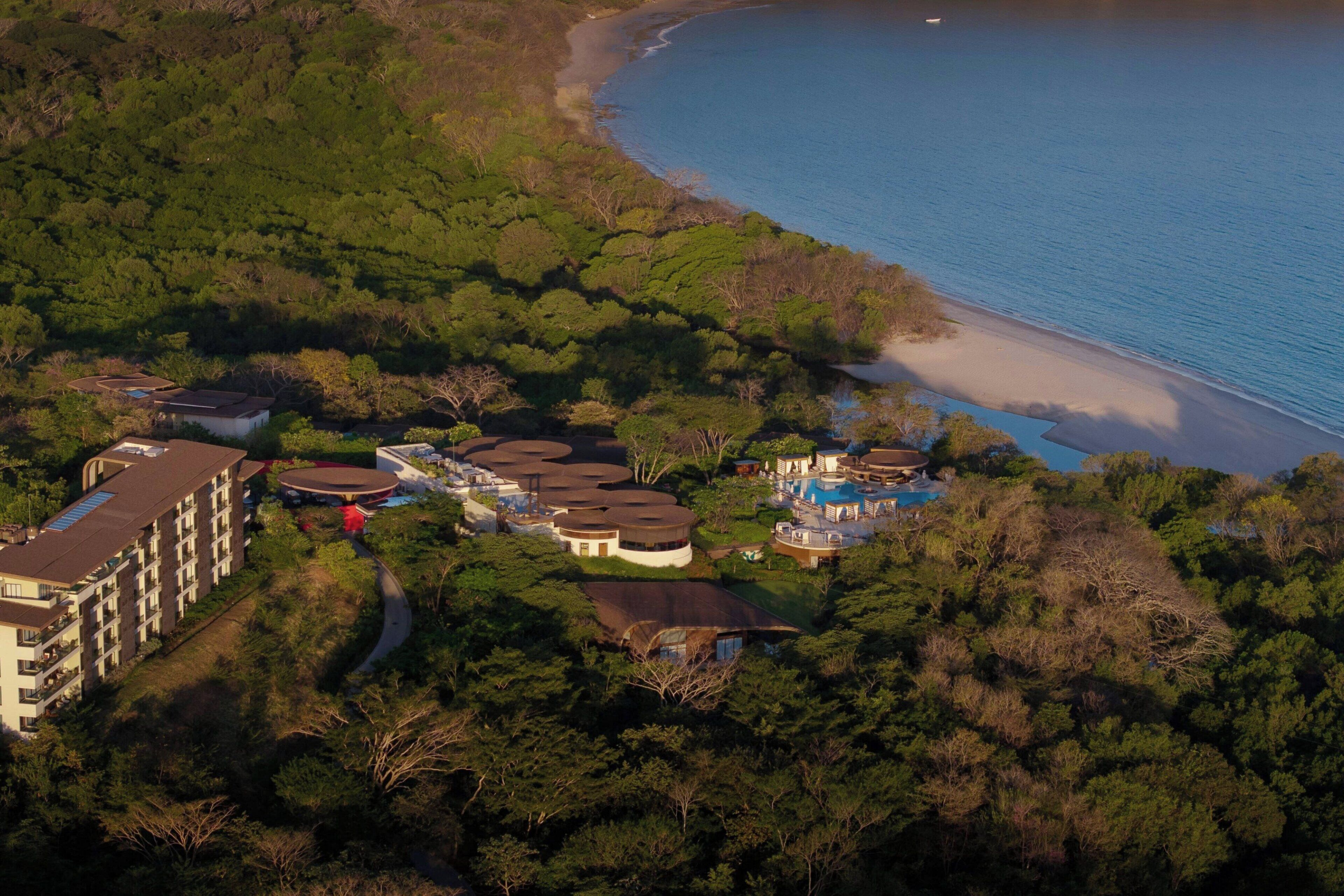 Luchtbeeld van een resort met meerdere gebouwen, een strand en een zwembad.