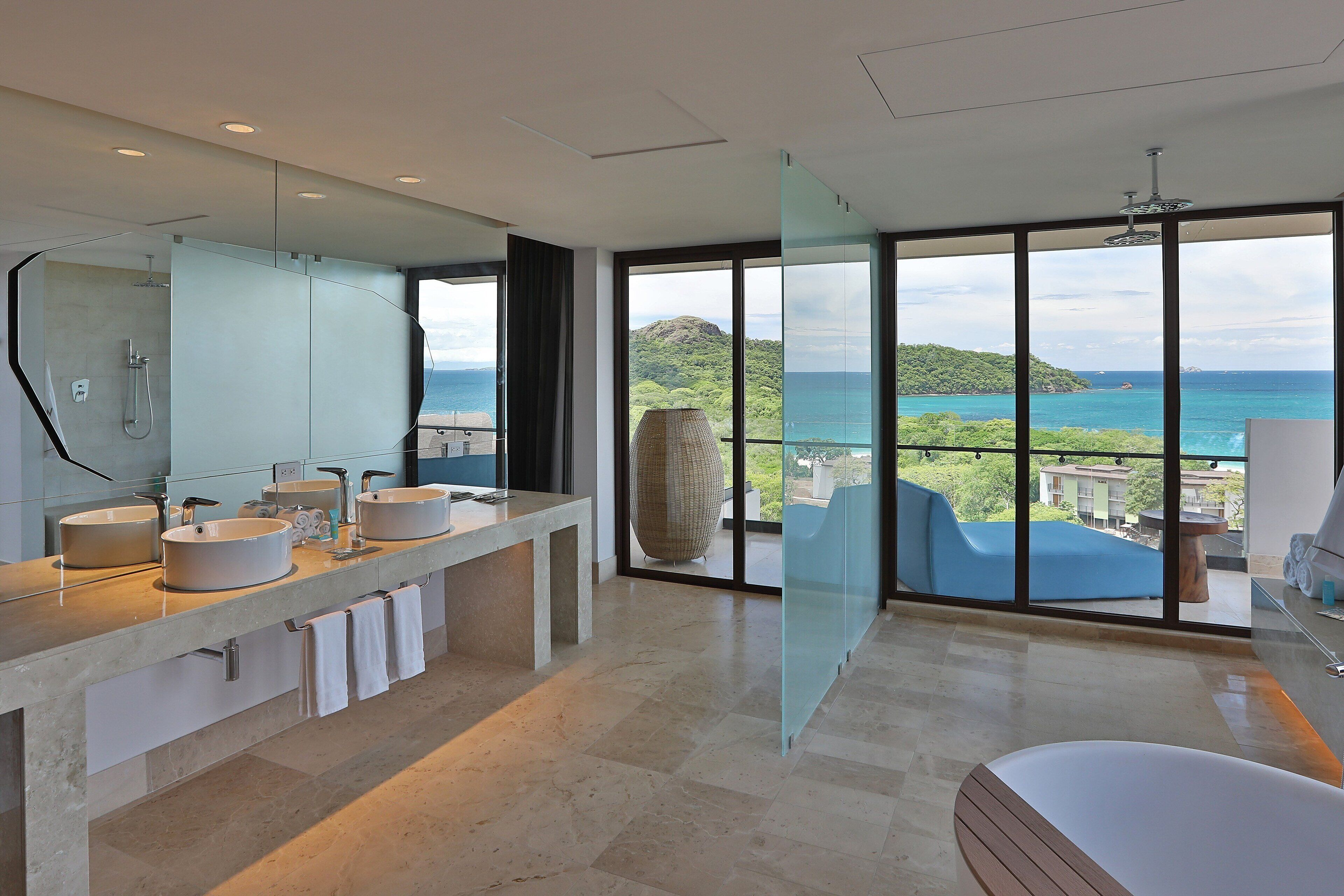 A modern bathroom with a large window, a bathtub, and a vanity with multiple sinks.
