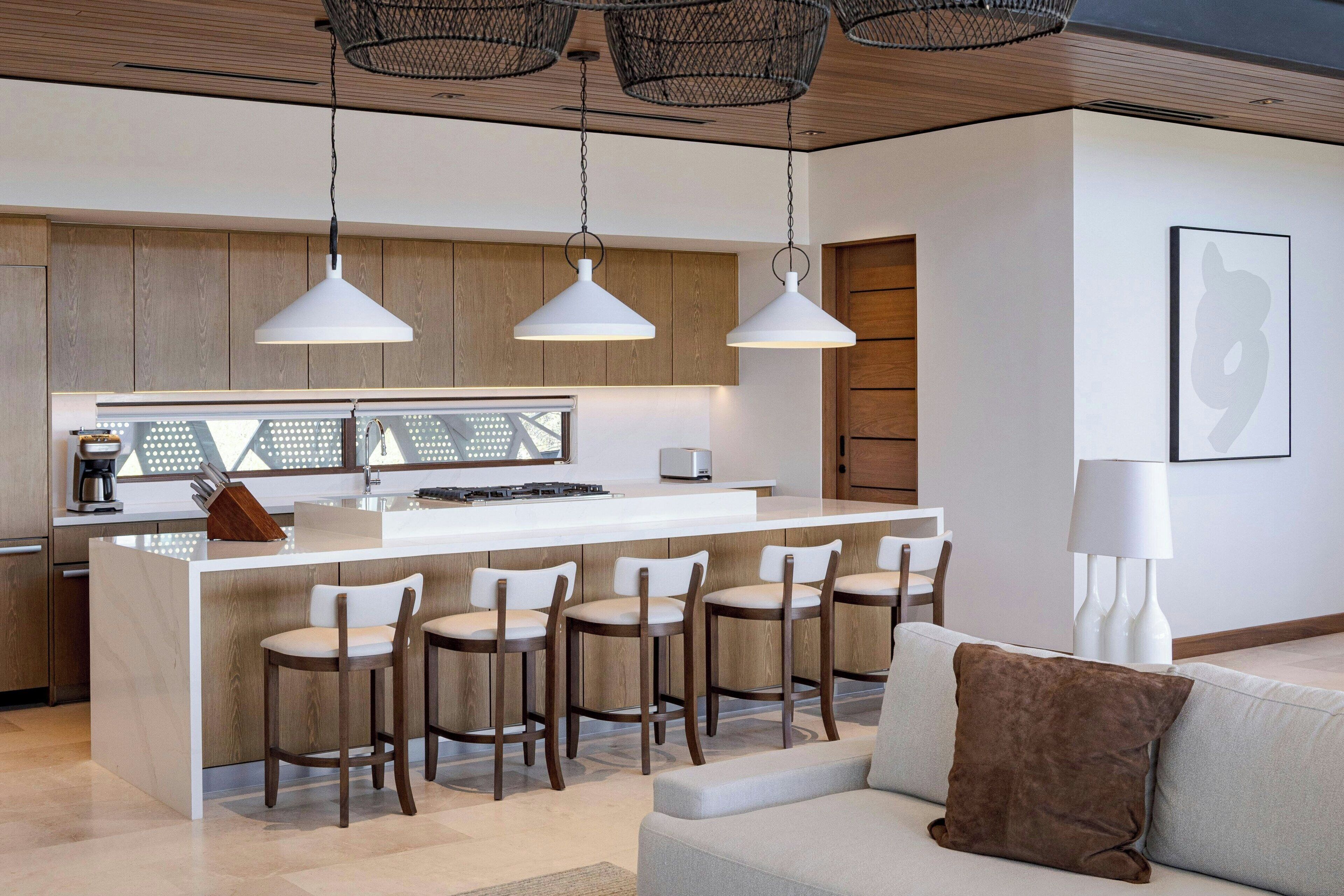 Una cocina moderna con una isla central, taburetes de bar, iluminación colgante y un diseño minimalista.