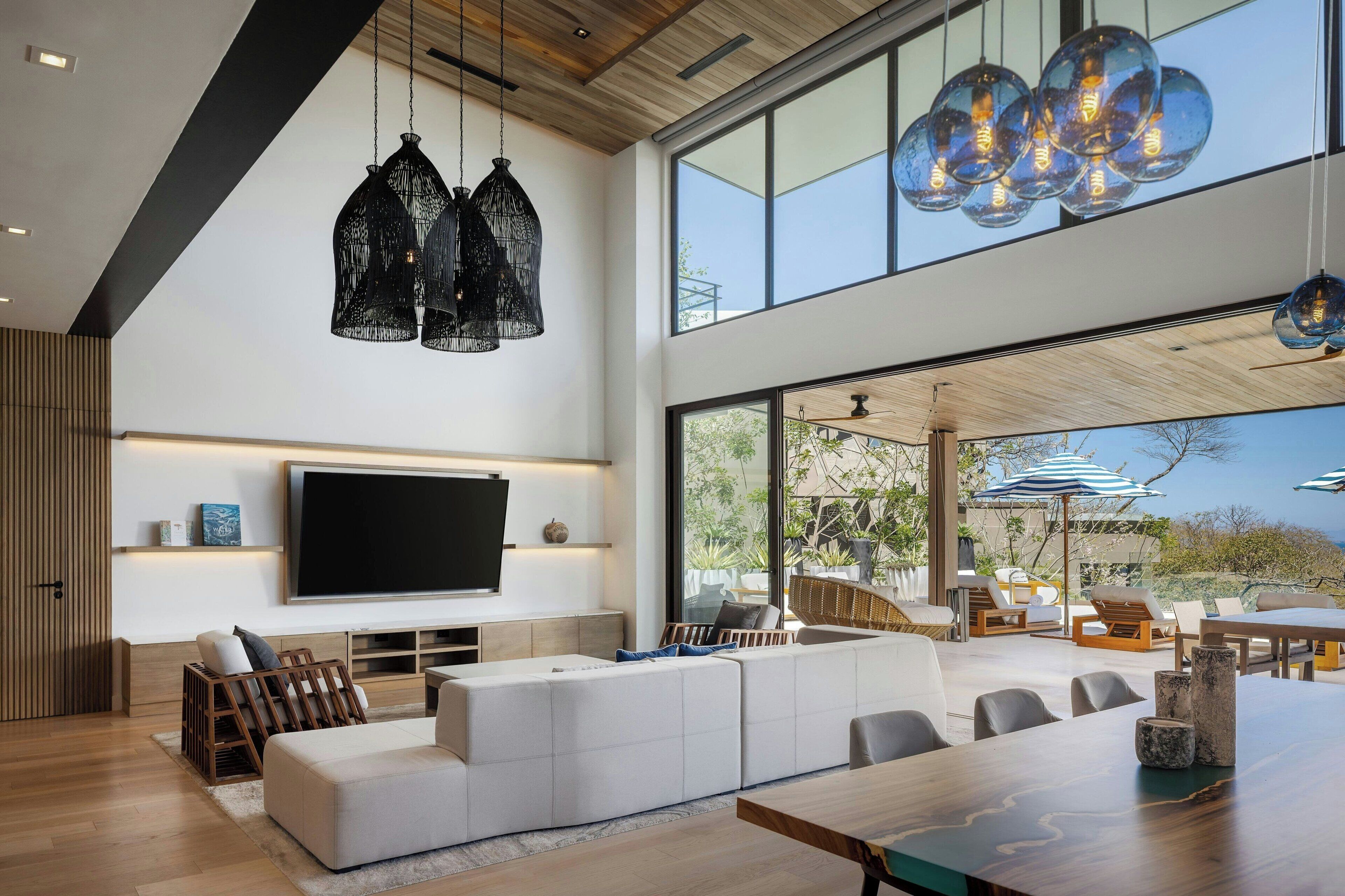 Una sala moderna con un televisor de pantalla plana grande, un sofá blanco modular y un comedor con mesa de madera.