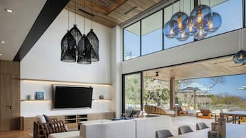 Una sala moderna con un televisor de pantalla plana grande, un sofá blanco modular y un comedor con mesa de madera.