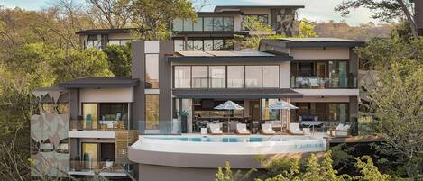 A multi-story modern house with a rooftop pool, outdoor seating, and a large glass facade.