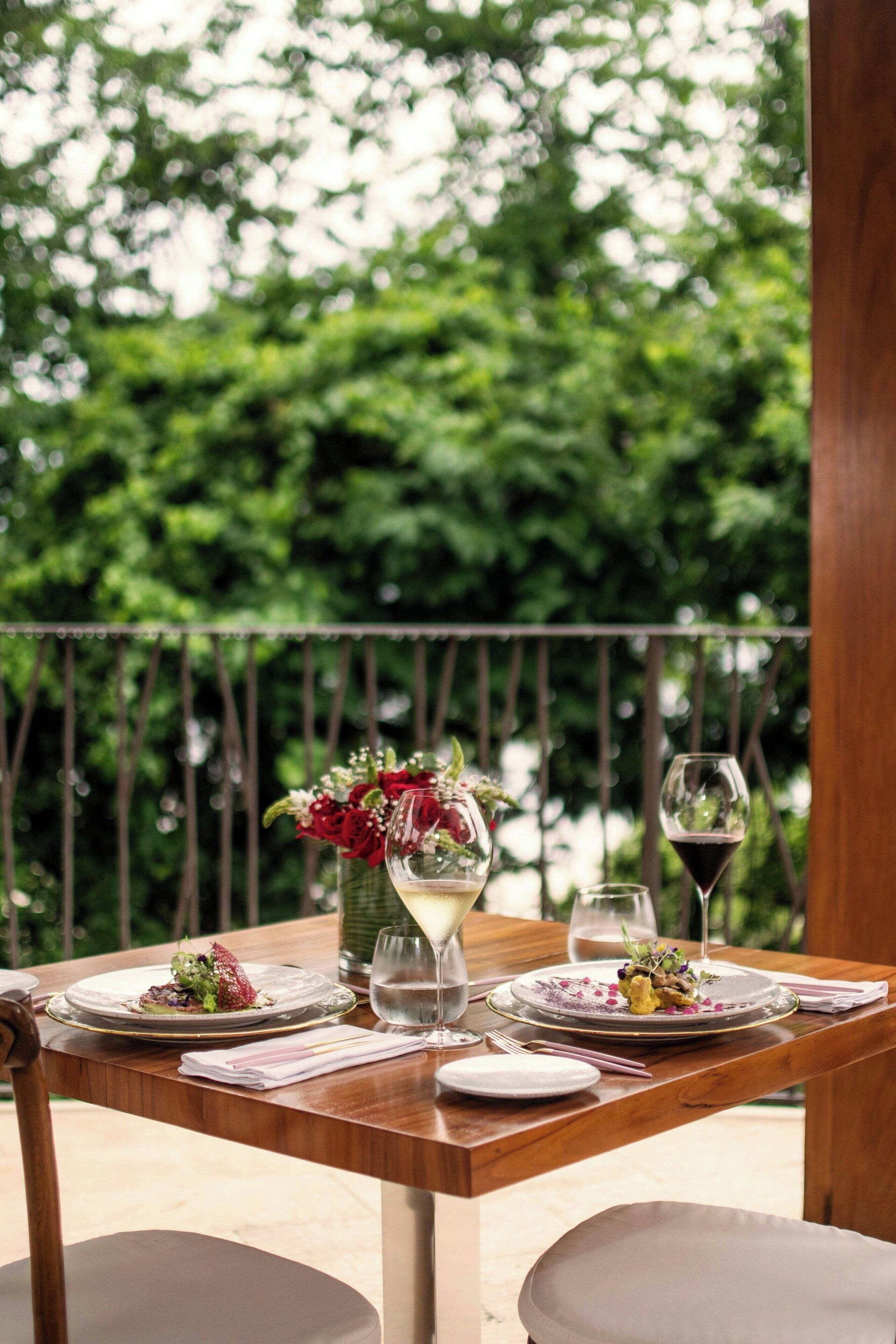 Una mesa de comedor al aire libre con platos de comida, vasos y un florero.