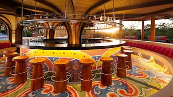 Una zona de bar con barra circular, taburetes de madera y un suelo con mosaicos de colores.