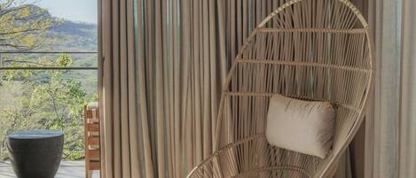 A modern room with a large window, a wicker chair, a wooden stool, and a view of the outdoors.