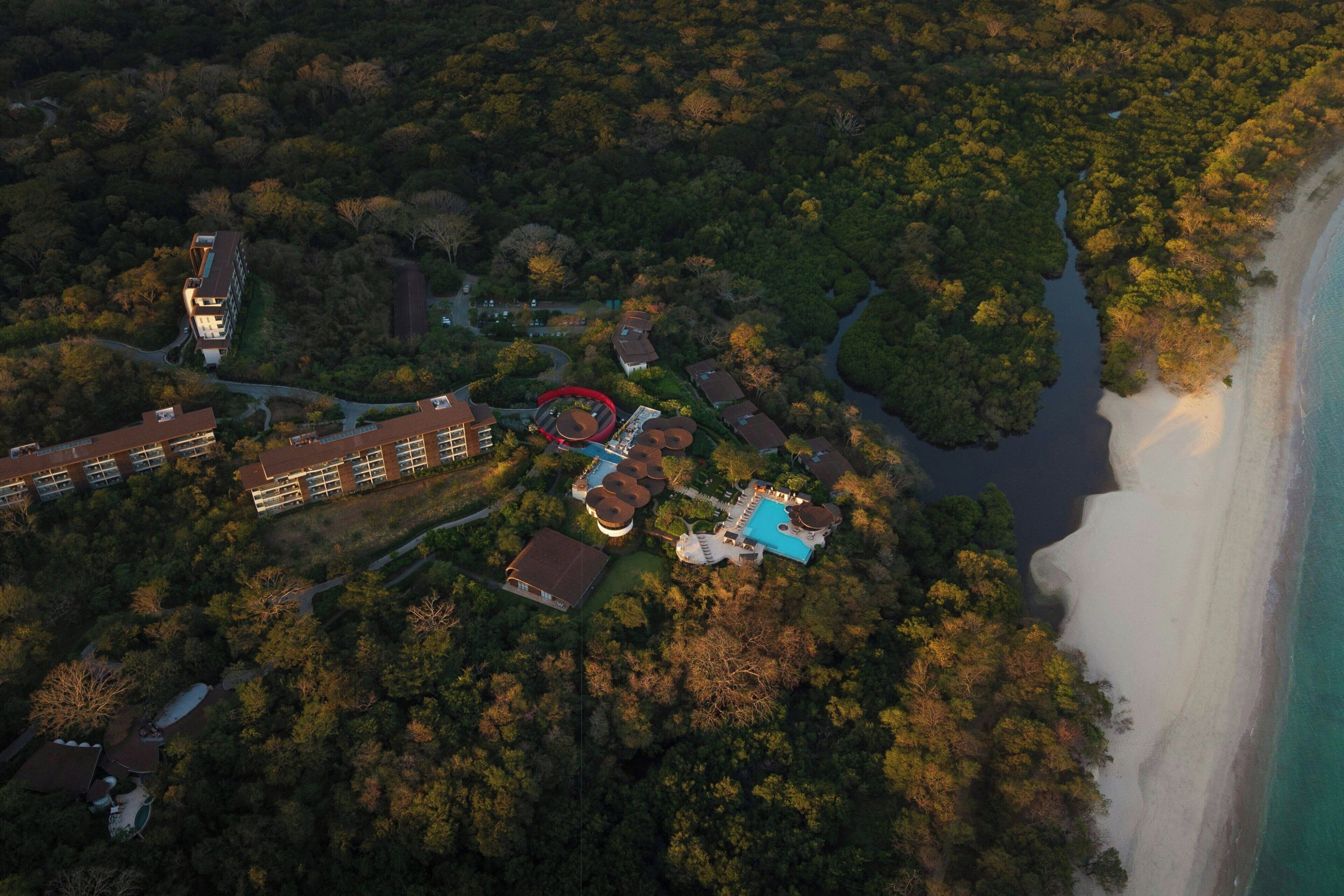 Luchtbeeld van een resort met meerdere gebouwen, een zwembad en een strand.