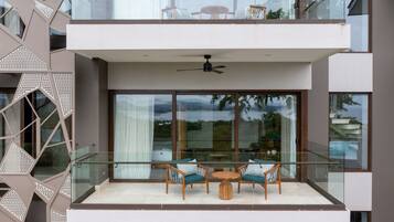 A modern balcony with glass railings, two wooden chairs, a small round table, and a ceiling fan.