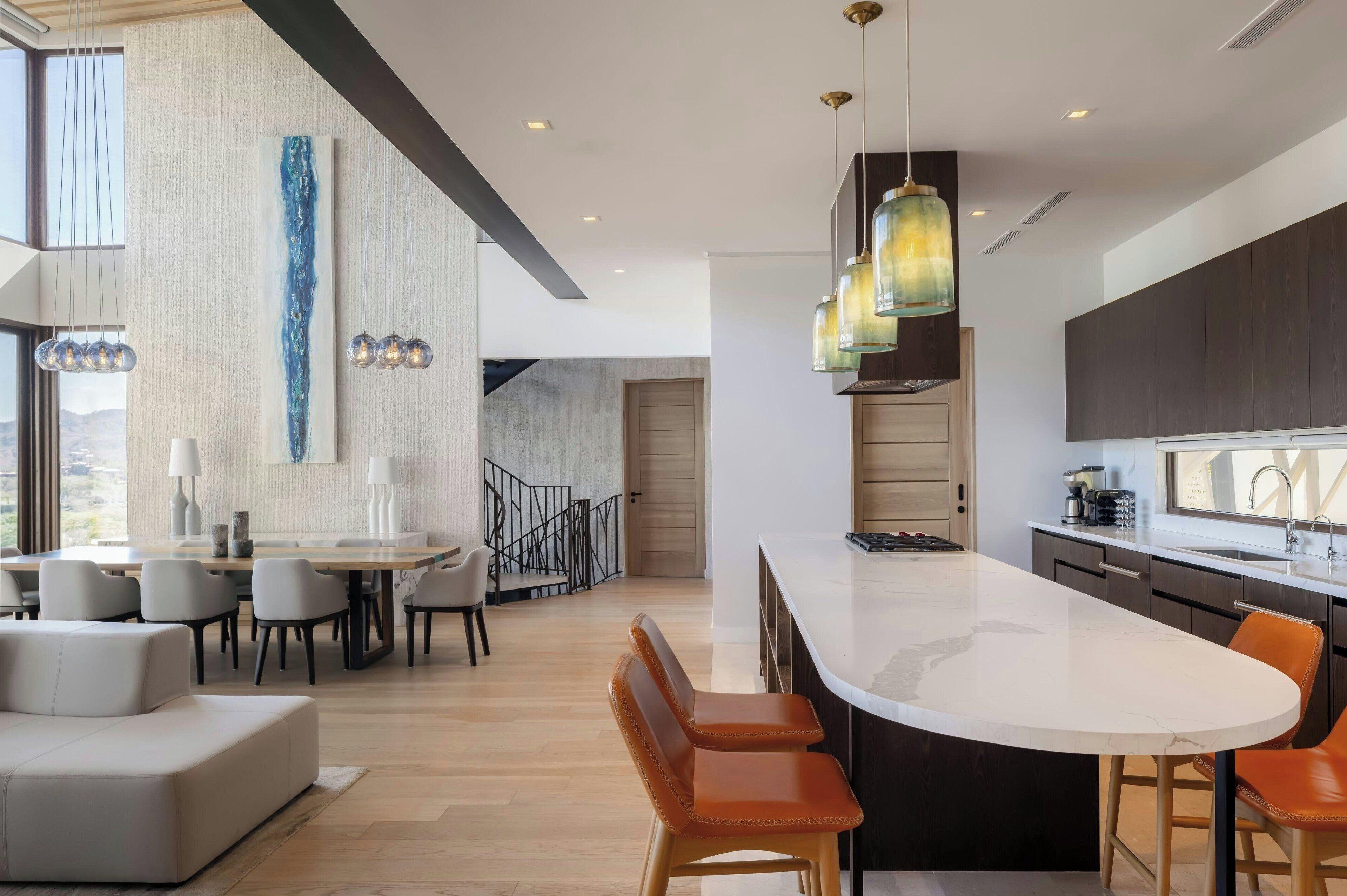A modern kitchen with a large island, pendant lighting, and a dining area with a sofa and chairs.