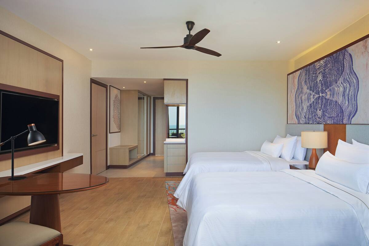 Ein Hotelzimmer mit zwei Betten, einem Schreibtisch, einem Fernseher und einem Deckenventilator.