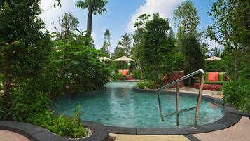 A pool area with a tiled deck, surrounded by lush greenery and outdoor seating with umbrellas.