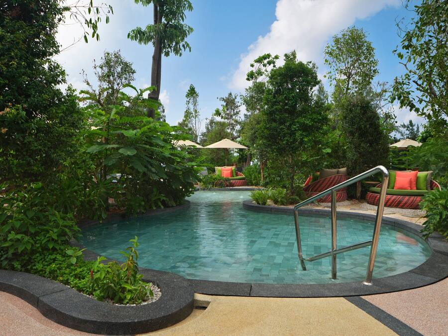 A pool area with a tiled deck, surrounded by lush greenery and outdoor seating with umbrellas.