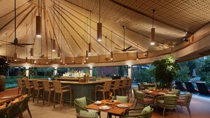 An outdoor dining area with multiple tables and chairs, a bar, and a ceiling with hanging lights. - The Westin Desaru Coast Resort (Bandar Penawar)