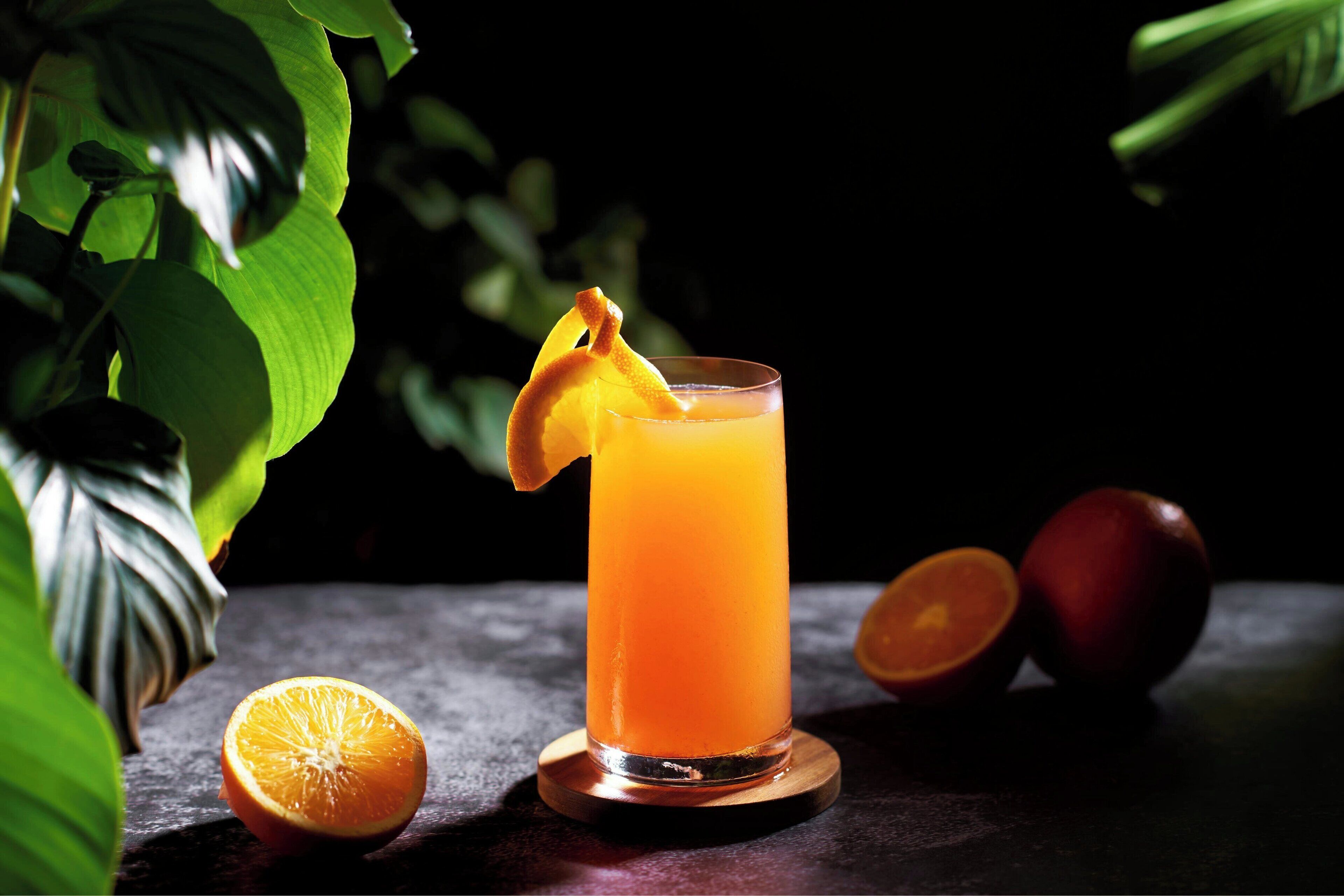 A glass of orange juice with a slice of orange on the rim, placed on a wooden coaster.