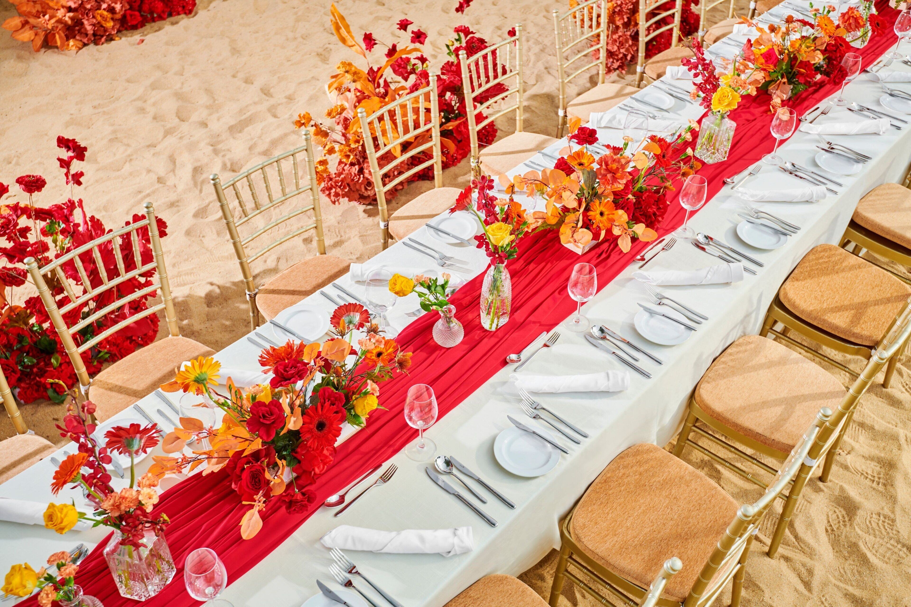 A long banquet table set with white tablecloths, red runners, and gold chairs.