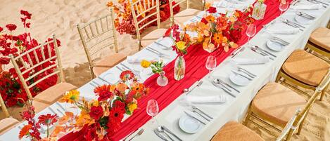 A long banquet table set with white tablecloths, red runners, and gold chairs.