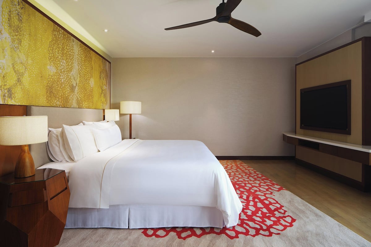 Ein Hotelzimmer mit Bett, Nachttischlampen, Deckenventilator, Fernseher und einem gemusterten Teppich.