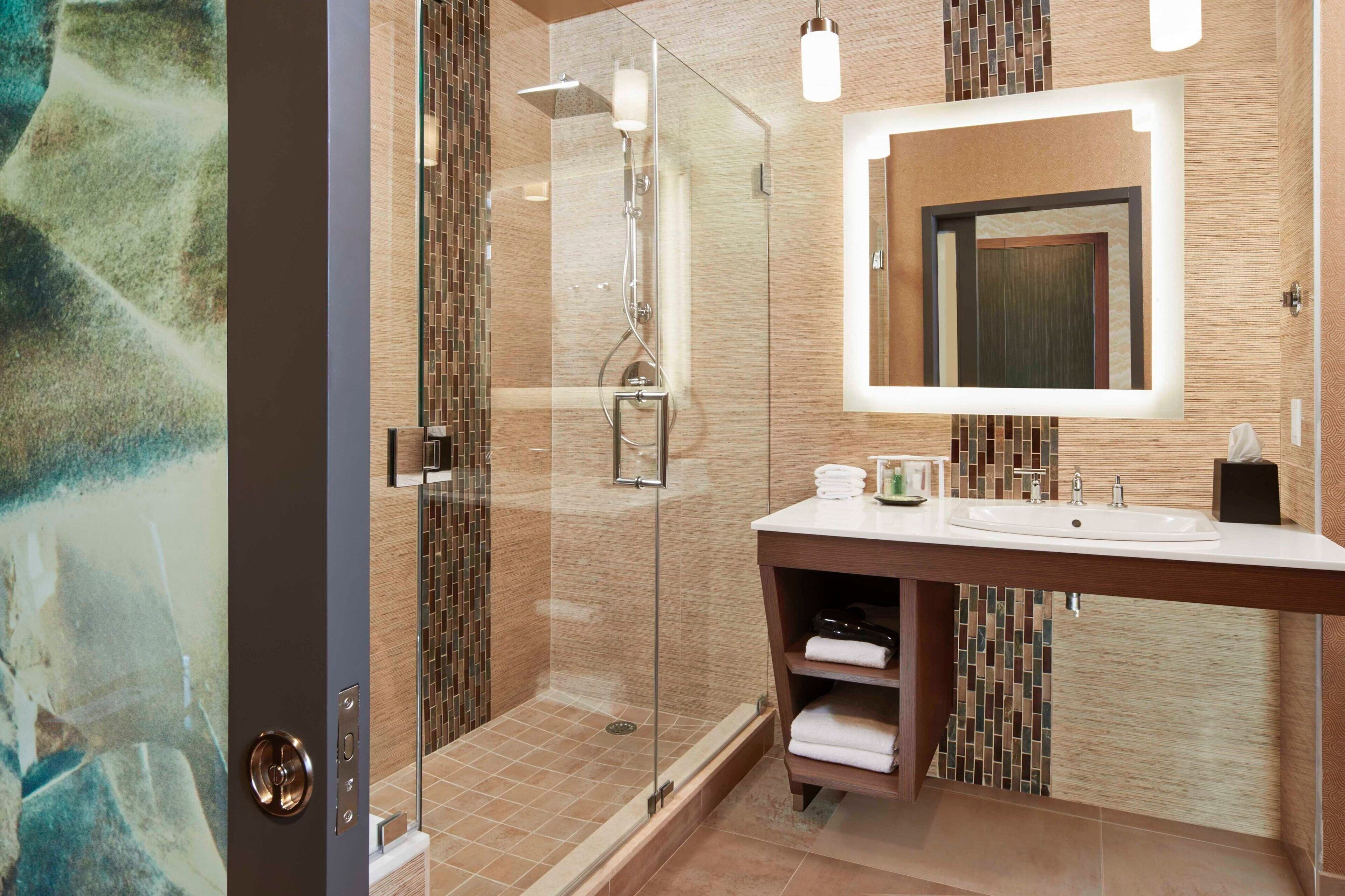 Un baño moderno con cabina de ducha acristalada, un espejo grande y un tocador con lavabo y barra para toallas.