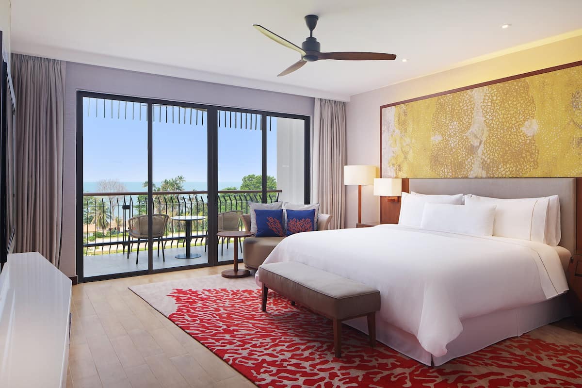 Ein Hotelzimmer mit einem großen Bett, einem Deckenventilator, einem Balkon mit Tisch und Stühlen sowie Blick ins Freie.