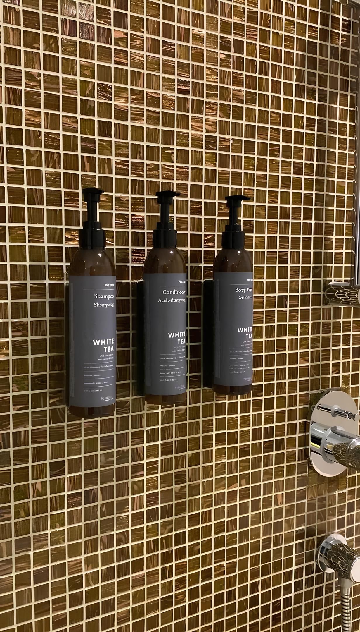 Three bottles of White Tea shampoo and conditioner on a tiled wall.