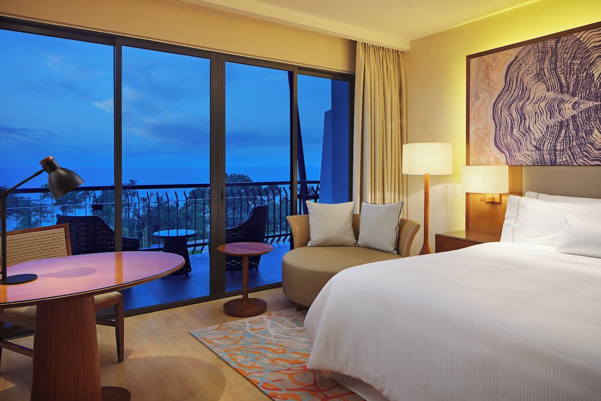 Ein Hotelzimmer mit einem großen Bett, einem Schreibtisch, einem Sessel und einem Balkon mit Stadtblick.