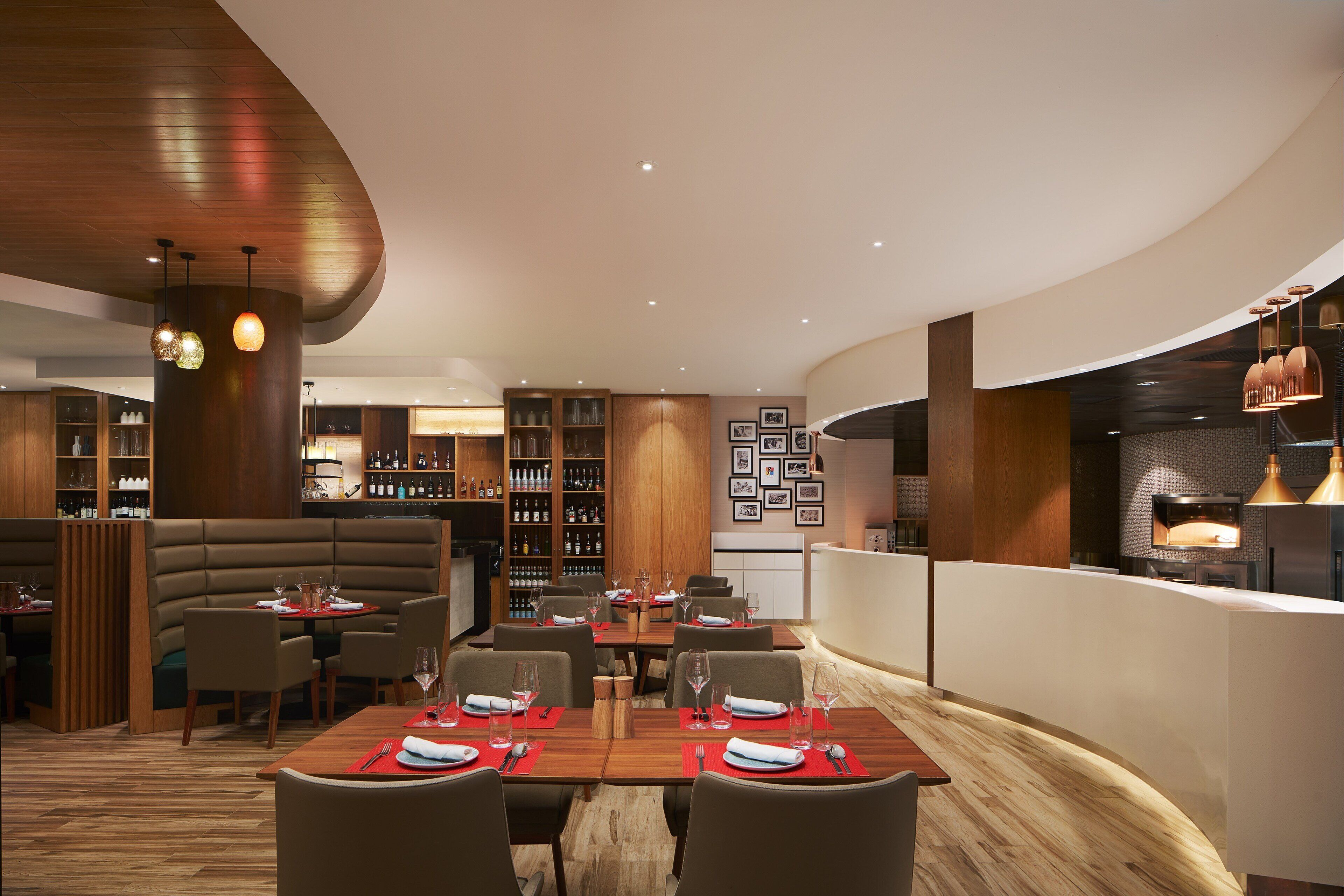 A modern restaurant with a curved ceiling, wooden furniture, and a bar area with a wine rack.