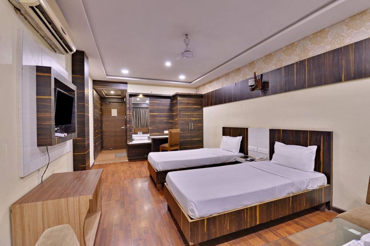 Quarto de hotel com duas camas, uma escrivaninha, televisão e chuveiro.