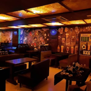 A dimly lit bar with wooden tables and chairs, a mural on the wall, and a sign indicating it's a sports bar. - Hotel puneet international (Raipur)