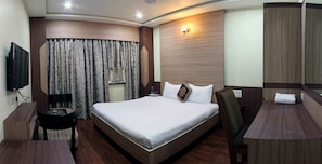 A hotel room with a large bed, a desk with a chair, a TV, and a window with curtains. - Hotel puneet international (Raipur)