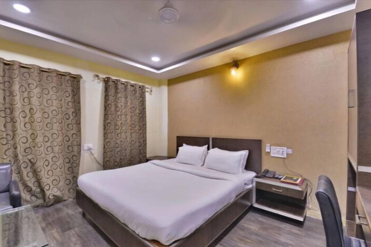 Quarto de hotel com uma cama, escrivaninha, cadeira e mesa de cabeceira.
