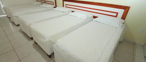 A room with three single beds, each with a wooden headboard and white bedding.