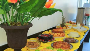 A buffet table with various desserts and fruits, a potted plant, and a beverage dispenser. - Rede Andrade Porto Seguro Navegantes (Porto Seguro)