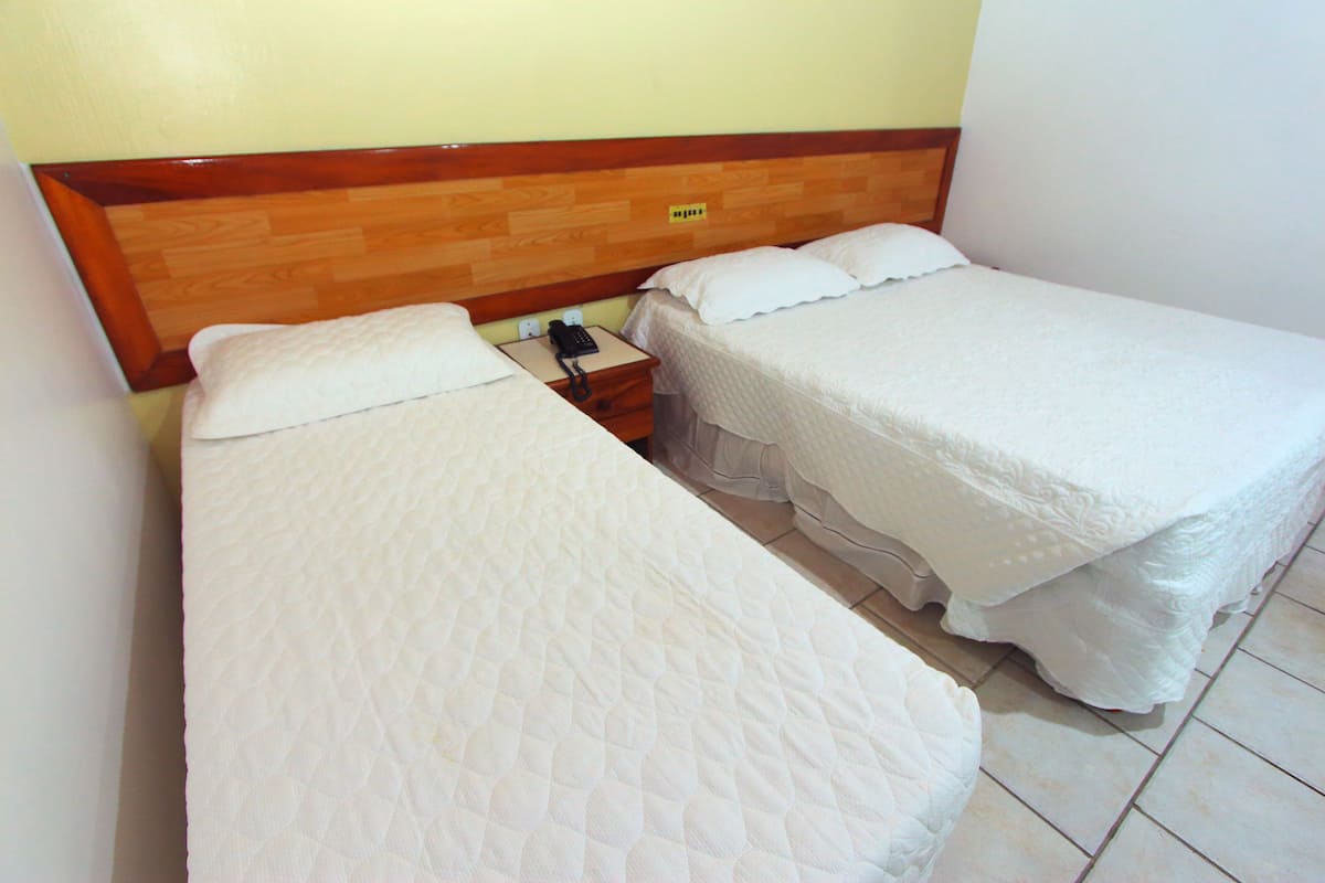 Una habitación con dos camas individuales, cabecero de madera, mesita de noche con teléfono y enchufe de pared.