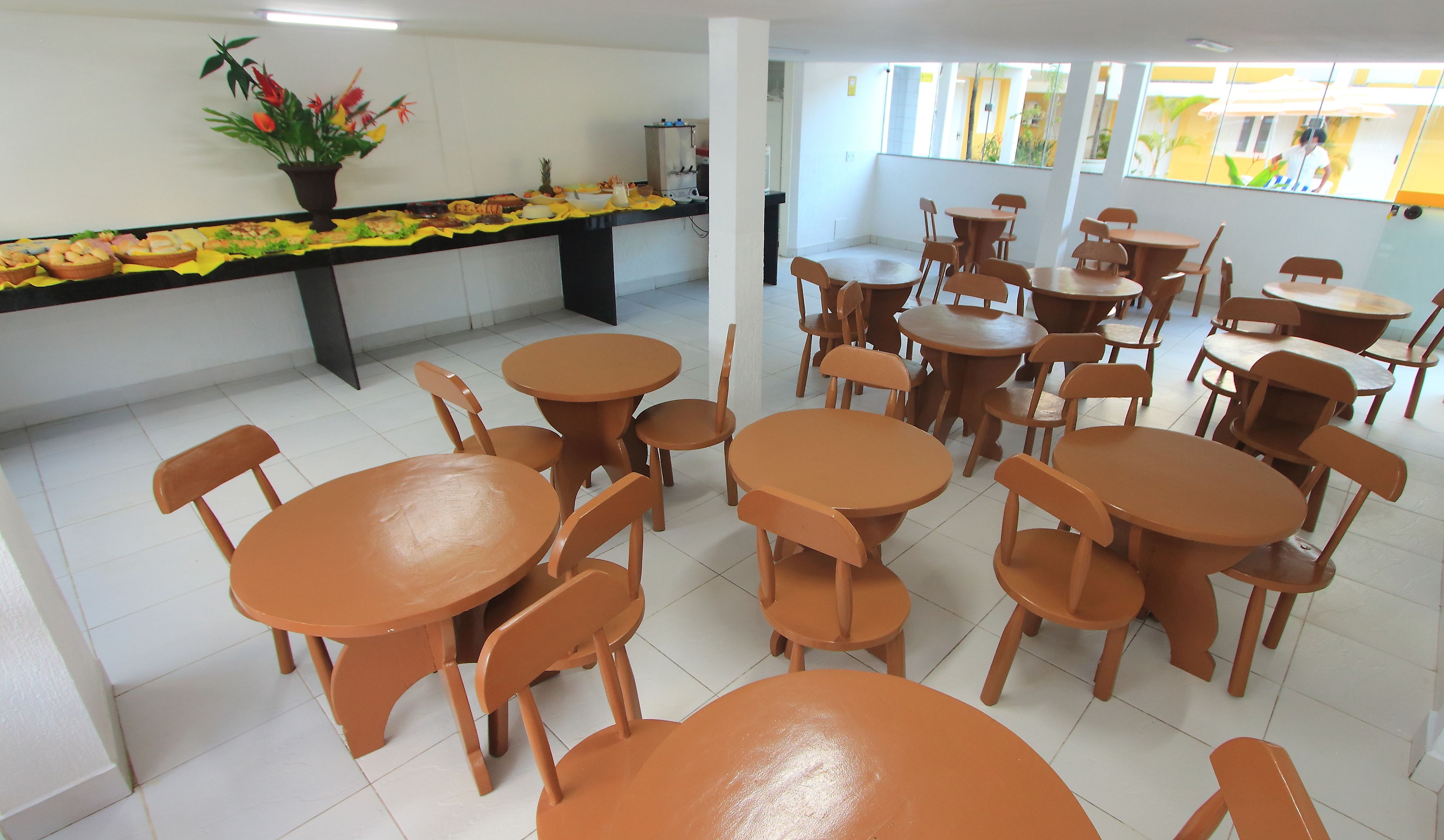 A cafeteria with round tables and chairs, a buffet counter with food, and a potted plant.
