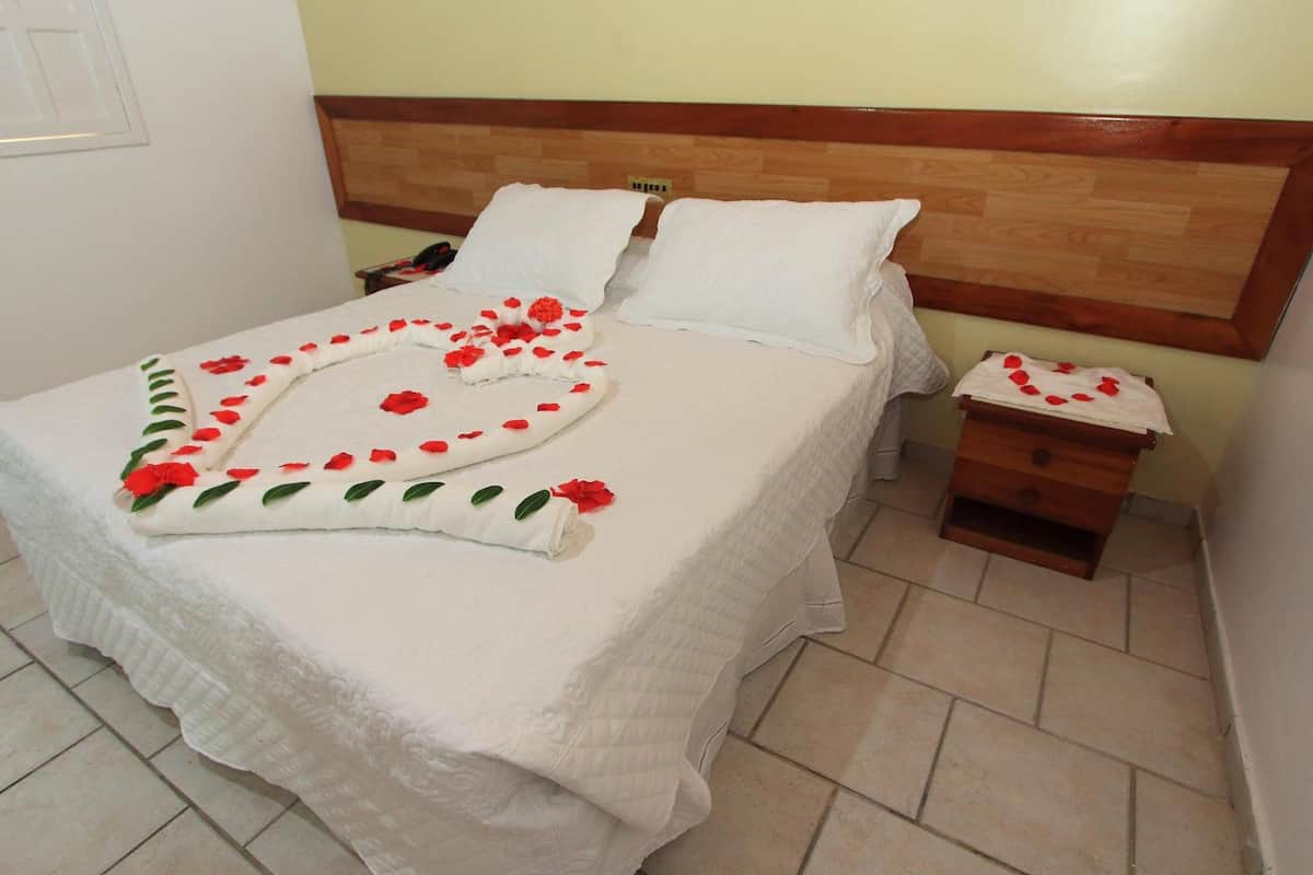 Una cama bien hecha con sábanas blancas y pétalos de rosa dispuestos sobre el edredón.