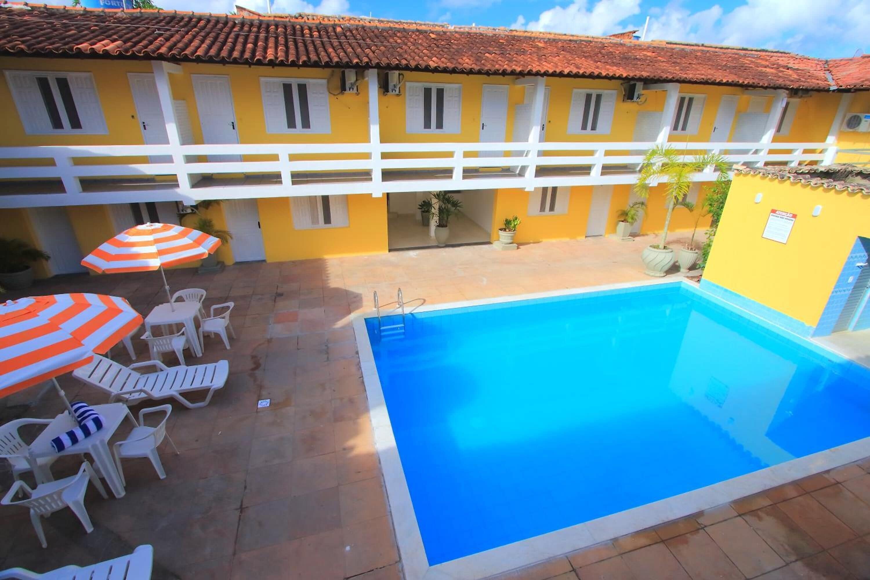 A yellow building with a red-tiled roof, a swimming pool, and outdoor seating with umbrellas.