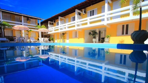 A hotel with a swimming pool, white railings, and outdoor seating with umbrellas. - Rede Andrade Porto Seguro Navegantes (Porto Seguro)