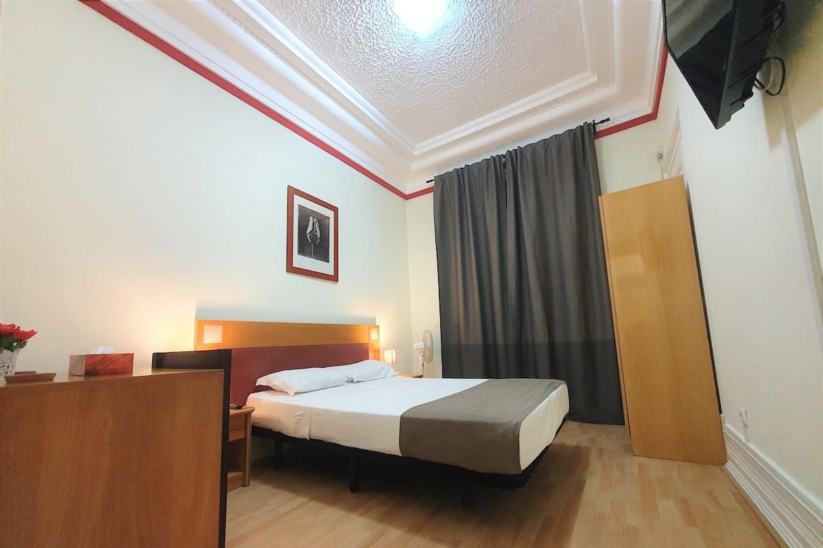 A hotel room with a bed, bedside table, lamp, and a framed picture on the wall.