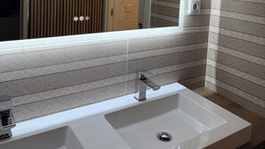 A modern bathroom with a large mirror, a white sink, and wooden paneling. - MIDIS - Local Accommodation (Lisbon)