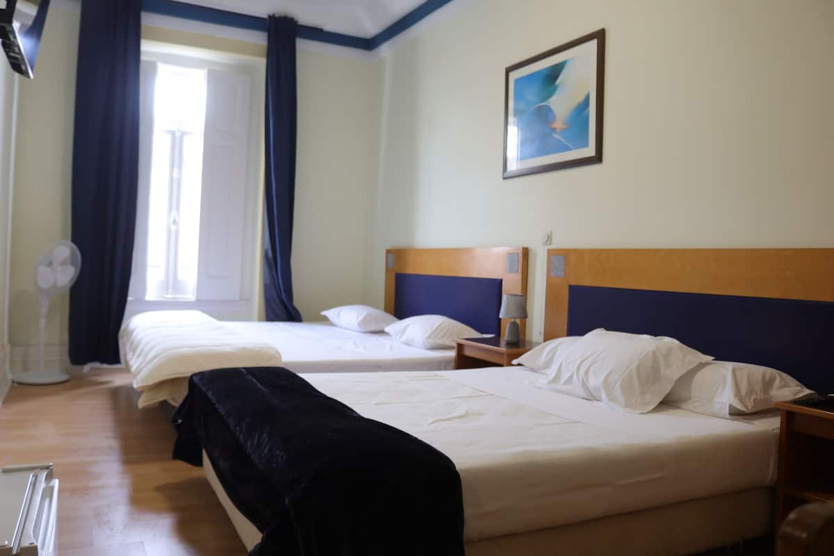 A hotel room with two beds, a ceiling fan, a window with curtains, and a framed picture on the wall.