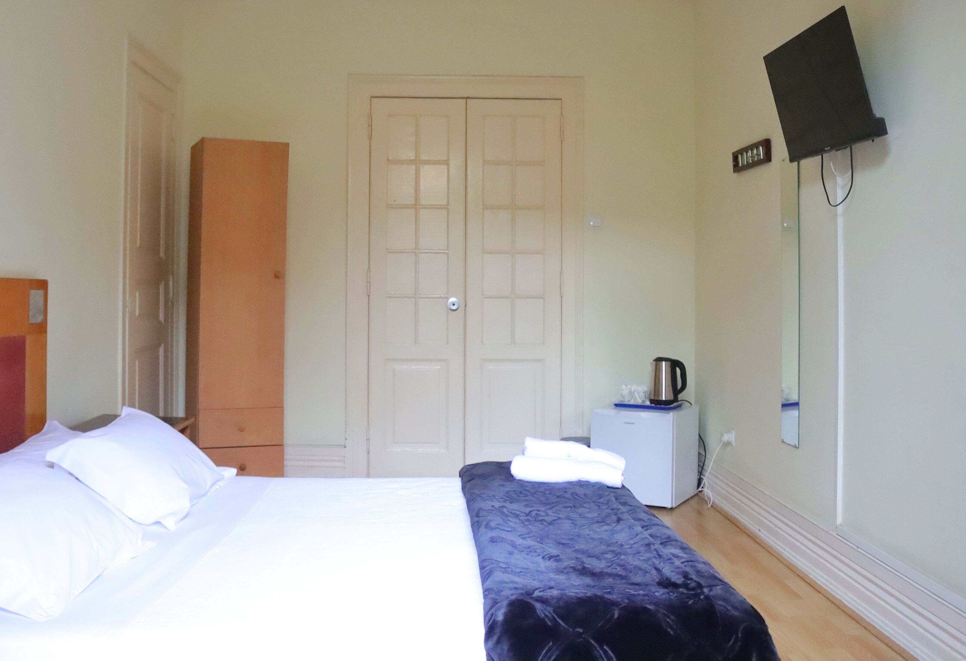 Een hotelkamer met een bed, een kledingkast, een kleine tafel met waterkoker en een flatscreen televisie aan de muur.