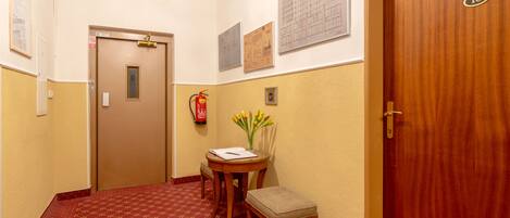 Un pasillo de hotel con un extintor, una mesita con un jarrón de flores y una puerta con el número 10.