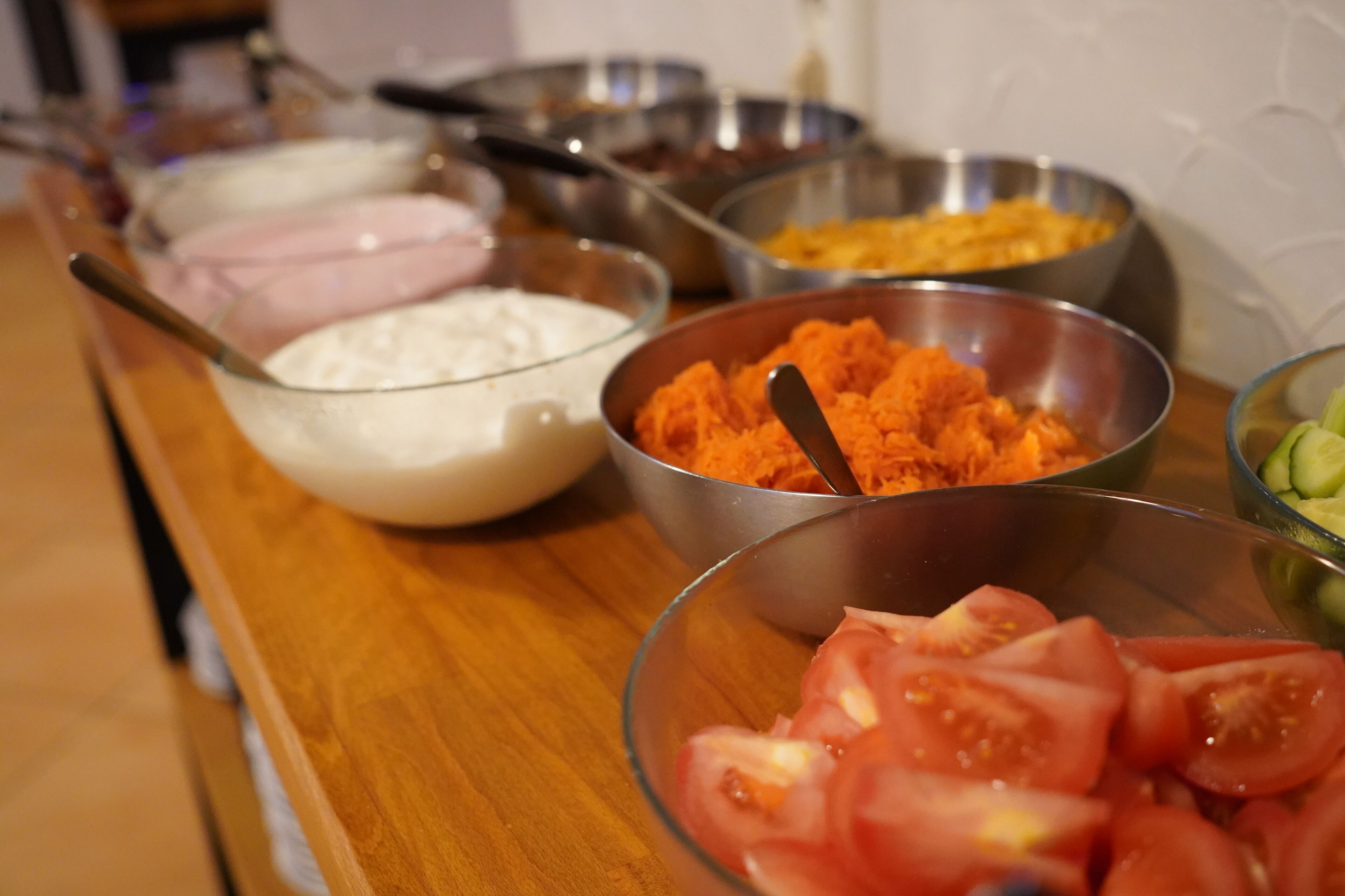 A buffet table with various food items including bowls of yogurt, carrots, and tomatoes.