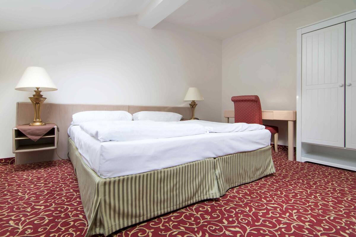 A hotel room with a bed, two bedside tables with lamps, a desk, and a wardrobe.