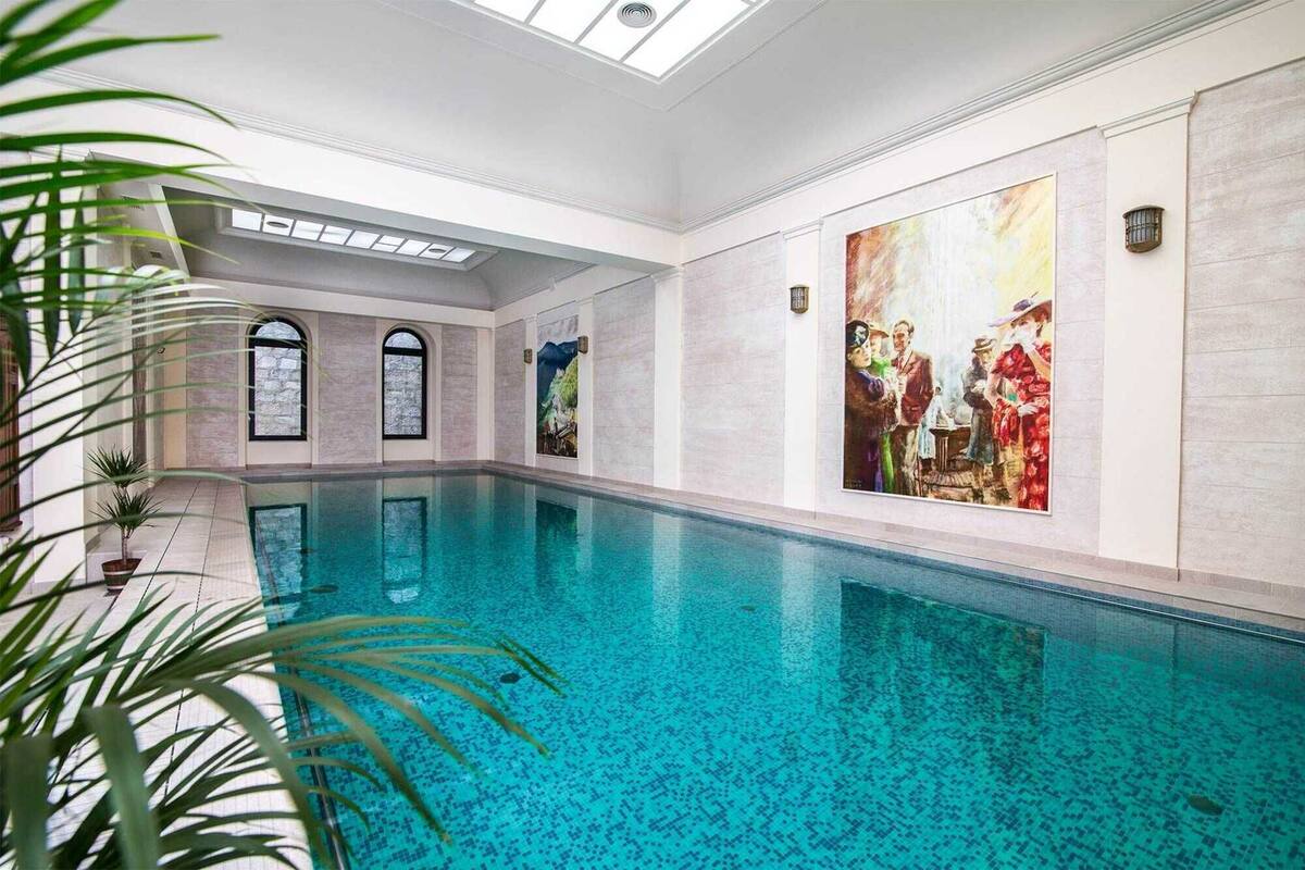 An indoor swimming pool with clear blue water, surrounded by white walls and a large painting.
