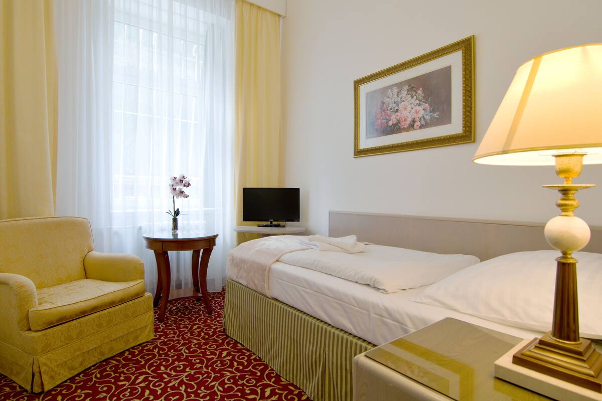 A hotel room with a bed, a chair, a TV, a lamp, and a painting on the wall.