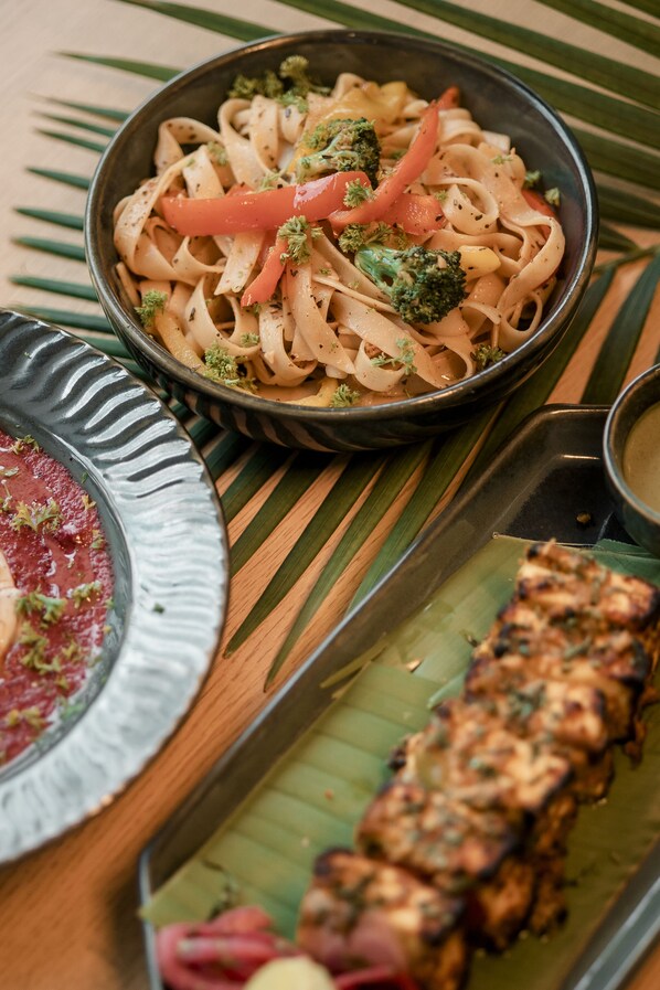 A meal with noodles, vegetables, and grilled meat on a wooden table with a banana leaf. - Hotel Broadway Udaipur (Udaipur)