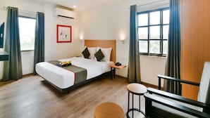 Habitación de hotel con cama, mesita de noche y un pequeño rincón de descanso con una silla y un taburete.